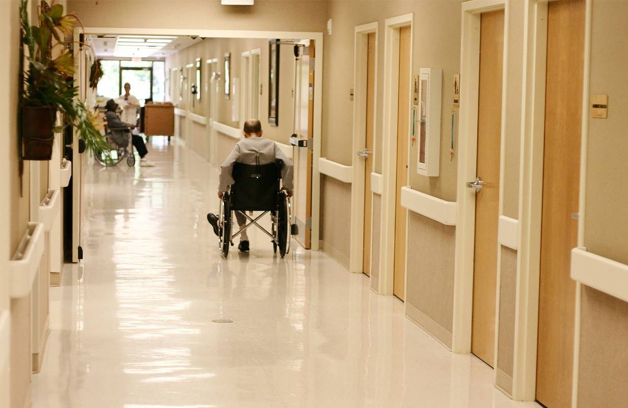 A man sitting in a wheel chair in the hallway of a nursing home. Next Avenue, nursing home reform