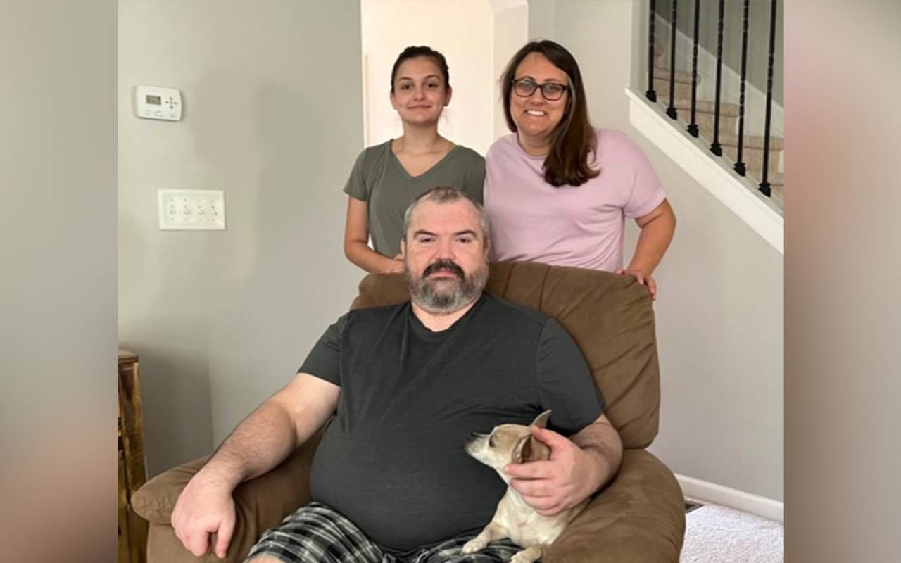 A man sitting on a chair with his dog surrounded by his family. Next Avenue, rare diseases