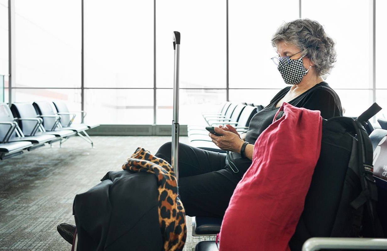 A person sitting in an airport on their cell phone. Next Avenue