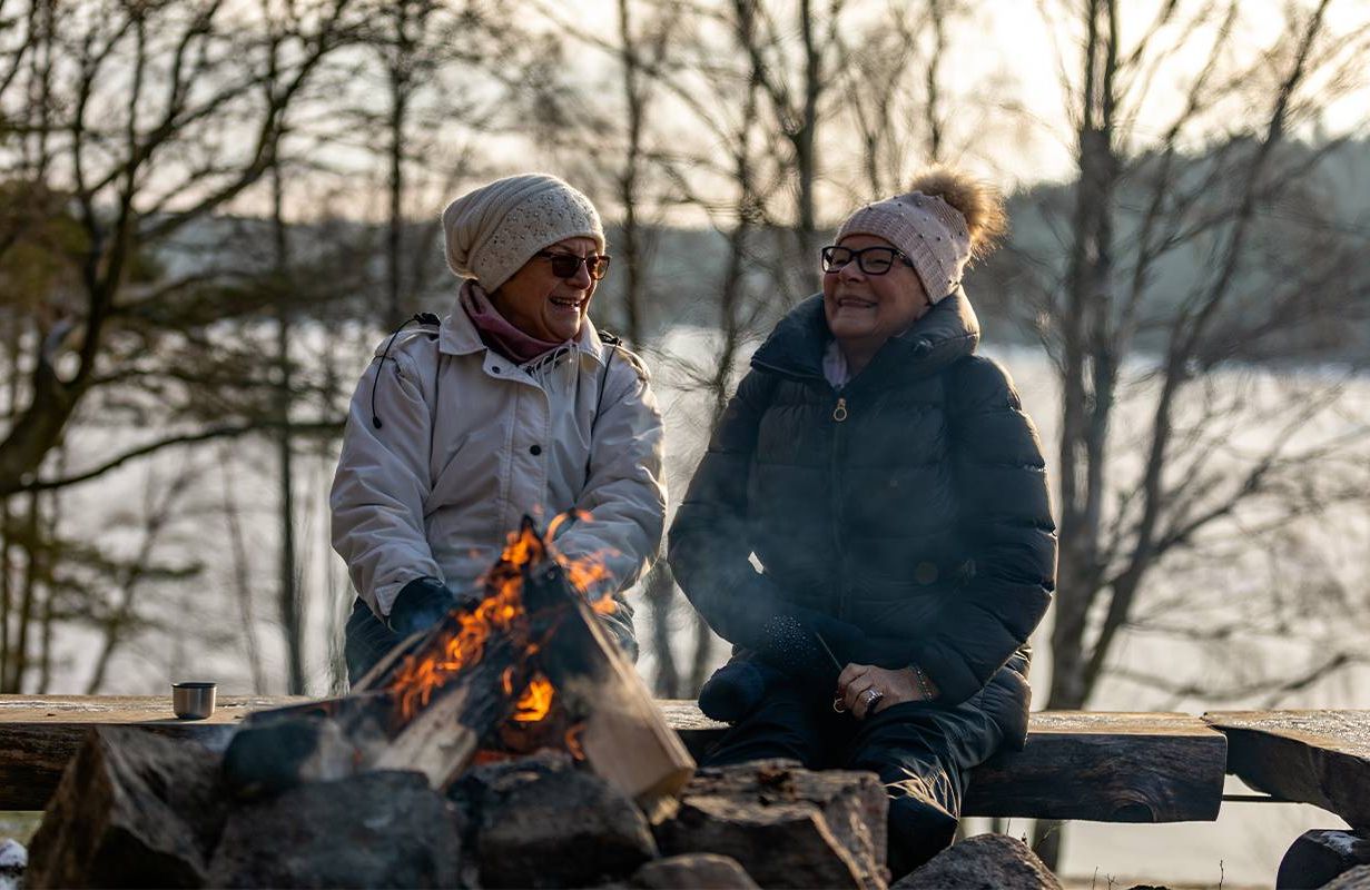 Two friends sitting by a bonfire. Next Avenue, getting through winter, hygge