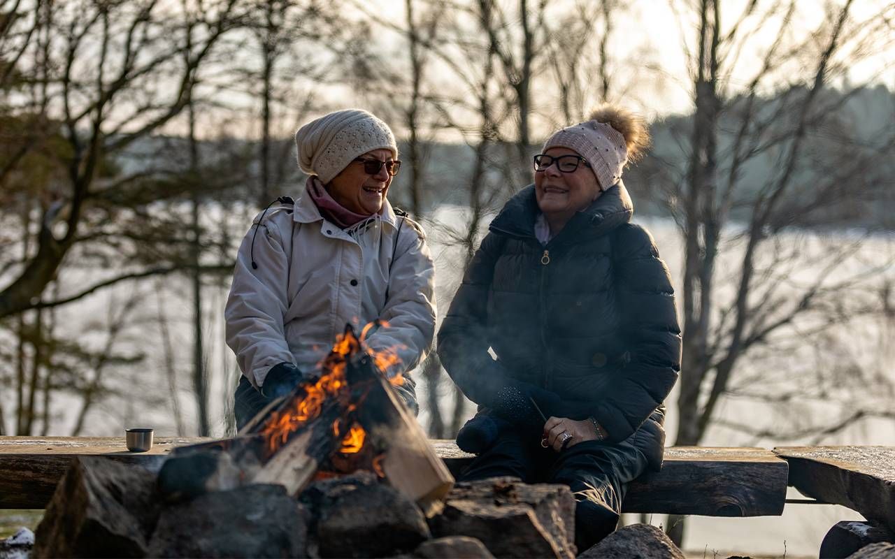 Two friends sitting by a bonfire. Next Avenue, getting through winter, hygge