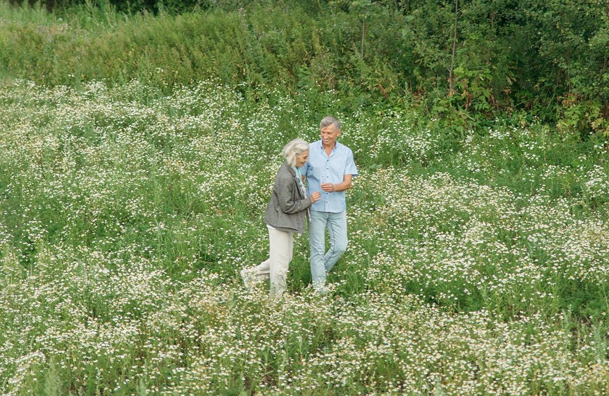 A couple walking in a field of flowers. Next Avenue, romance at midlife.