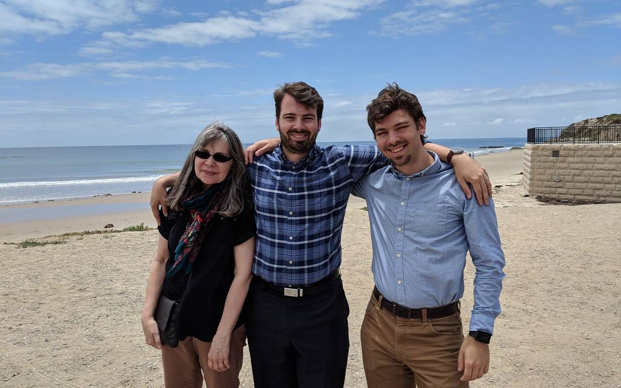 A woman standing on a beach with her two adult sons. Next Avenue, living simply, consuming less