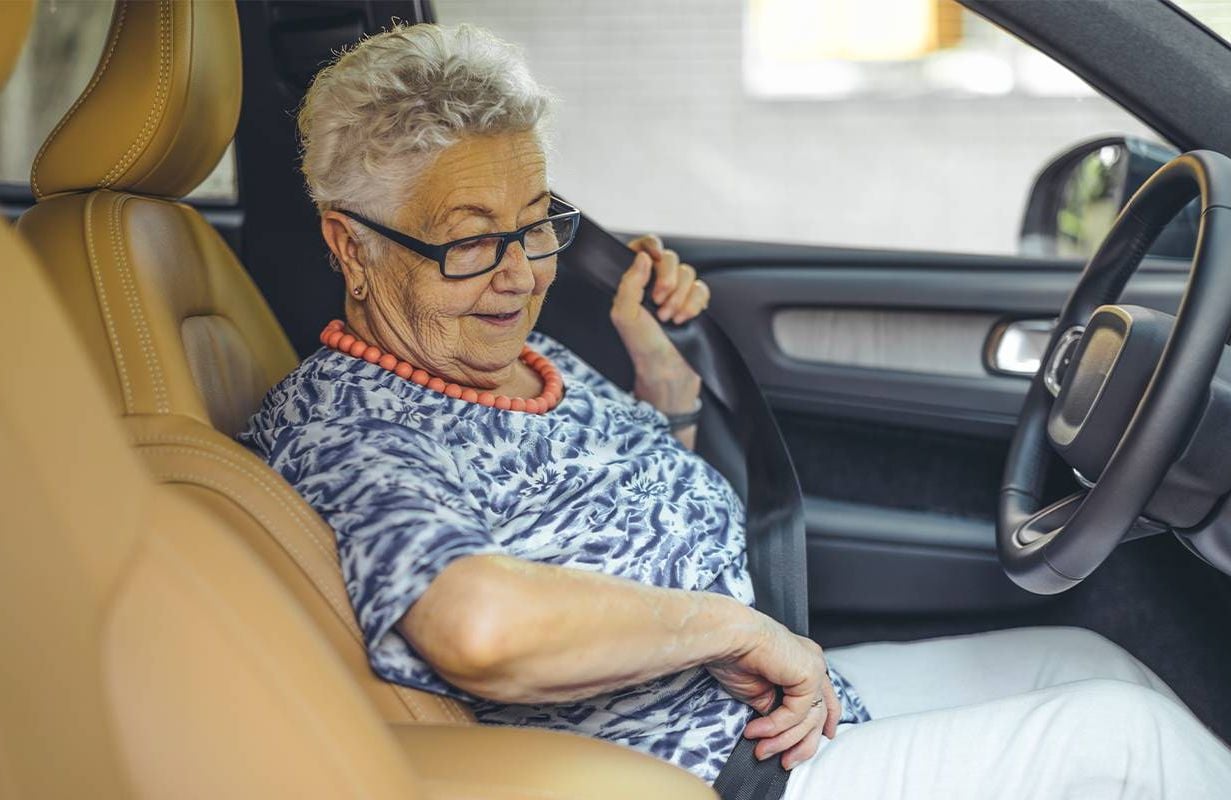 An older adult putting on their seat belt in the driver's seat.