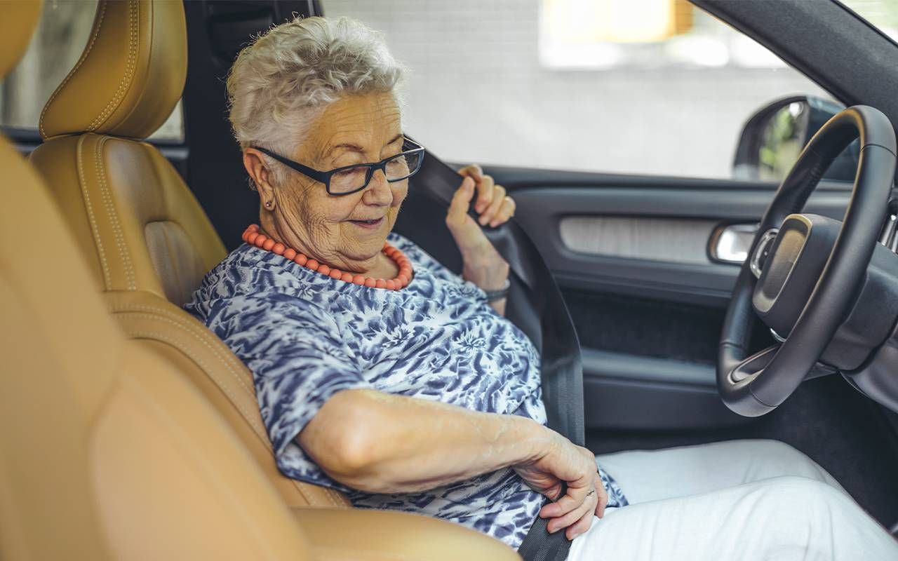 An older adult putting on their seat belt in the driver's seat.