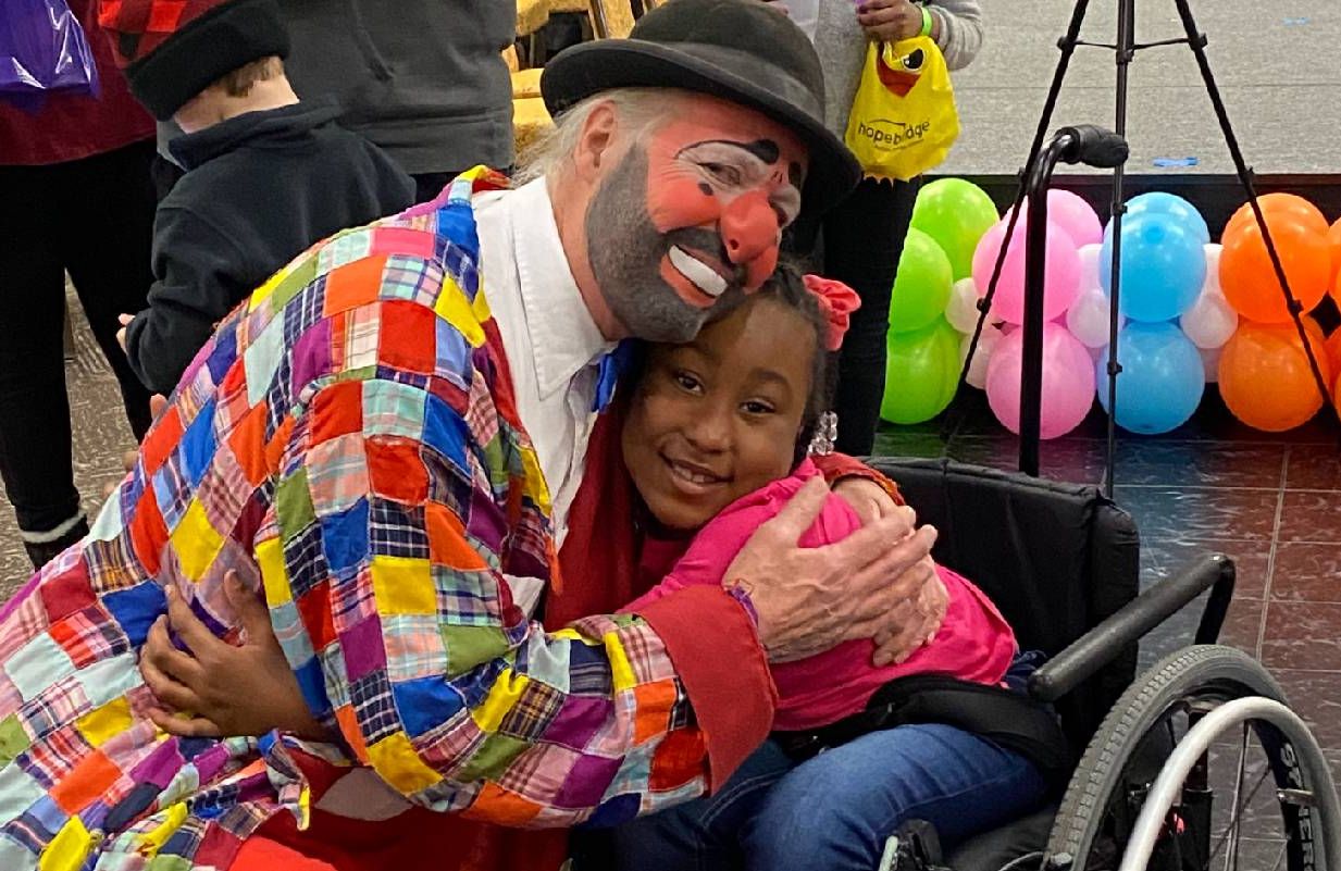 A man dressed as a clown hugging a young child. Next Avenue