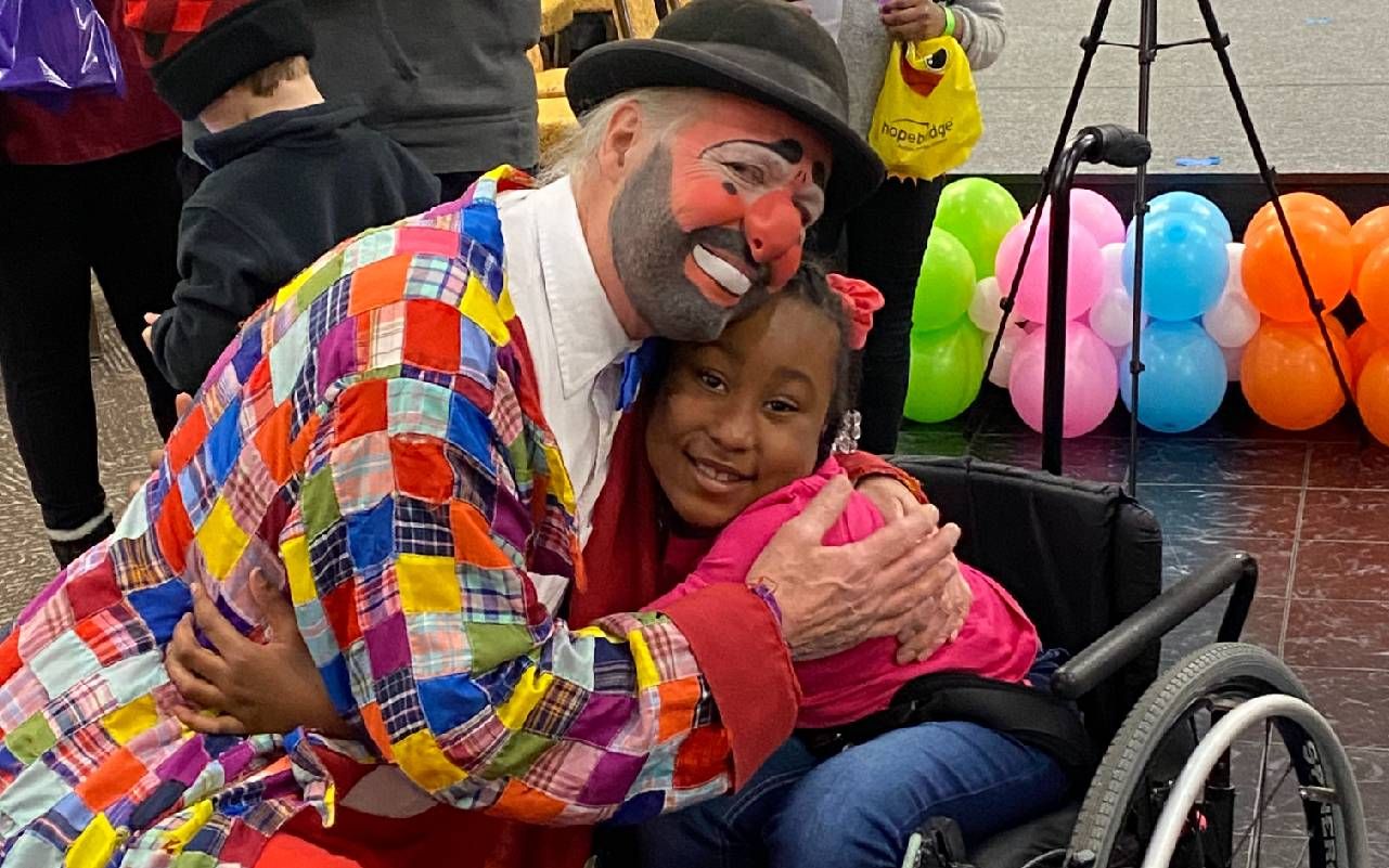 A man dressed as a clown hugging a young child. Next Avenue