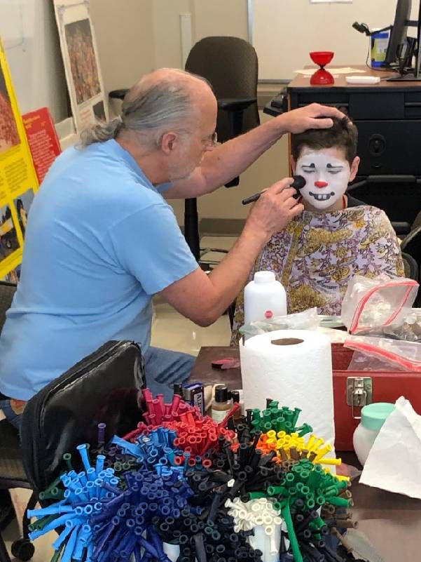 A man putting clown makeup on a young child. Next Avenue