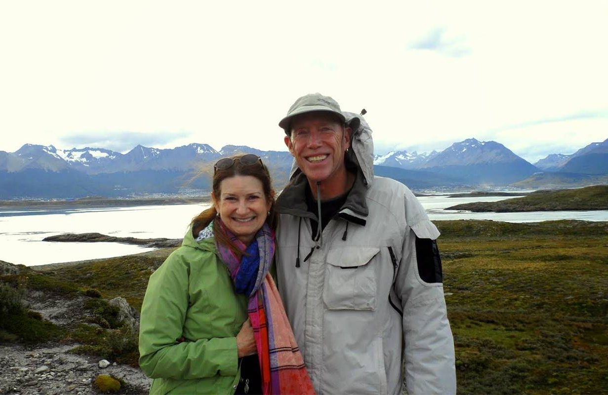 A couple standing in front of a large mountain range. Next Avenue, traveling on a budget