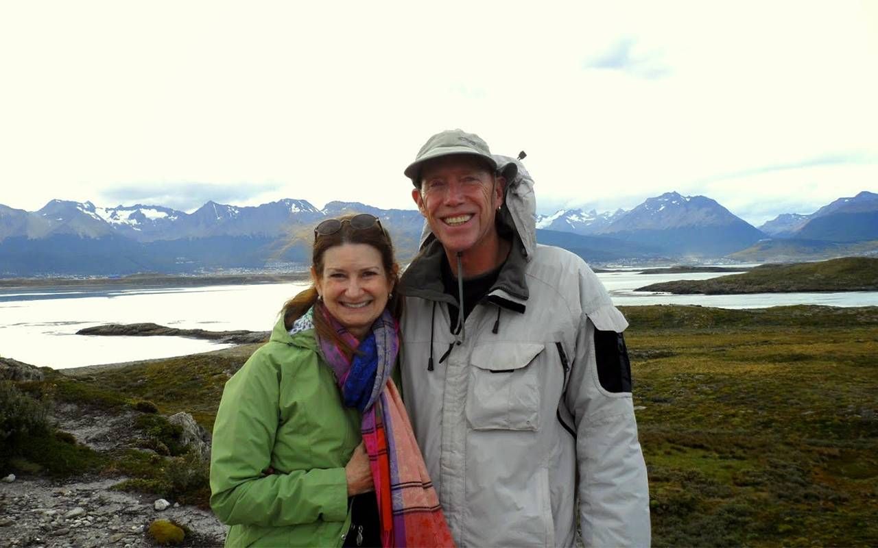 A couple standing in front of a large mountain range. Next Avenue, traveling on a budget