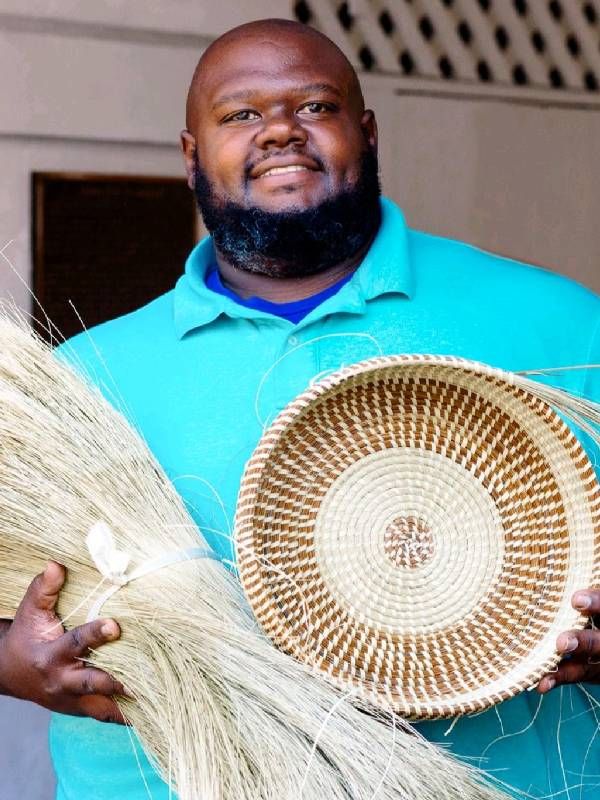 A man holding up a hand woven basket. Next Avenue, North and South Carolina arts
