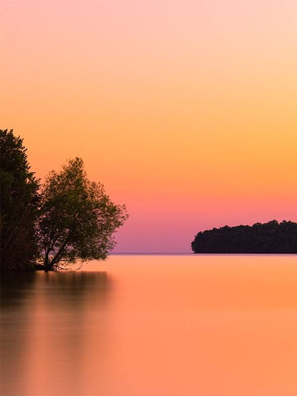 A pink and orange sunrise over a lake. Next Avenue, north american travel