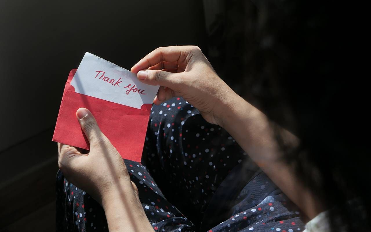 A person opening up a thank you card. Next Avenue