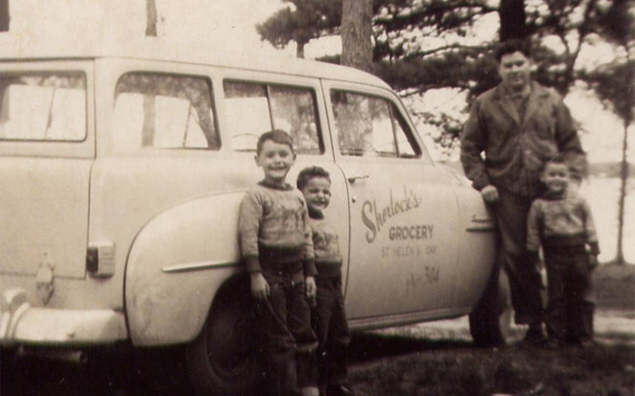 An old photo of a family standing outside of a van.