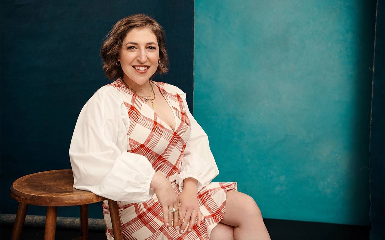 A person sitting on a stool in front of a backdrop. Next Avenue, PBS, Mayim Bialik