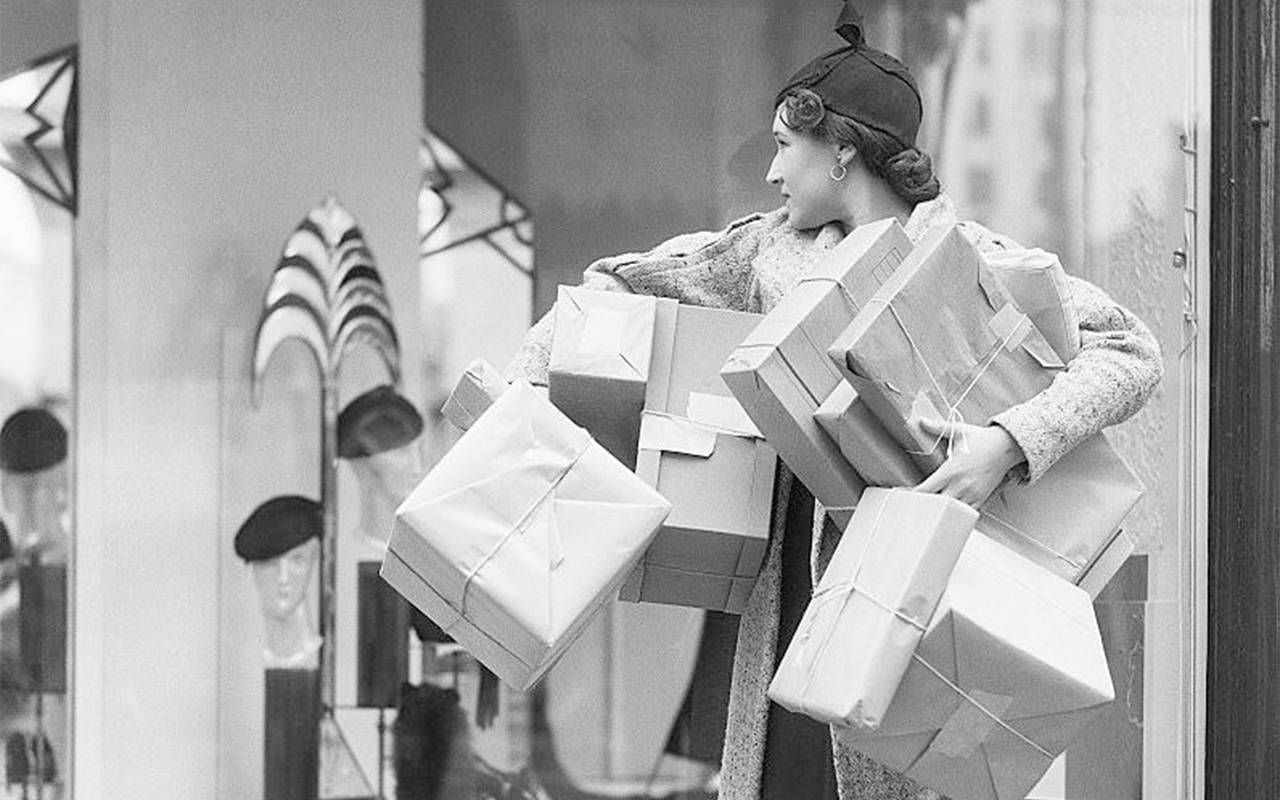 A vintage photo of a woman holding shopping boxes. Next Avenue