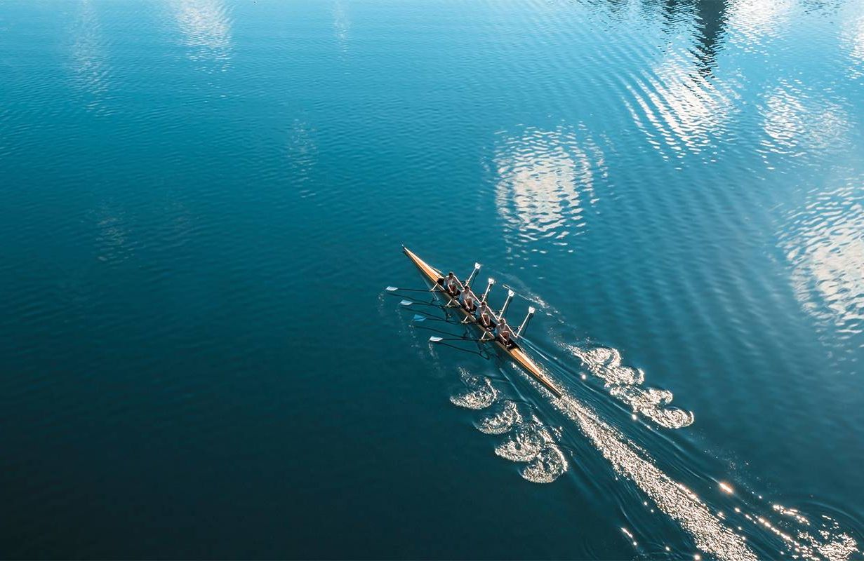 A rowing crew rows in a lake. Next Avenue, rowing after 50