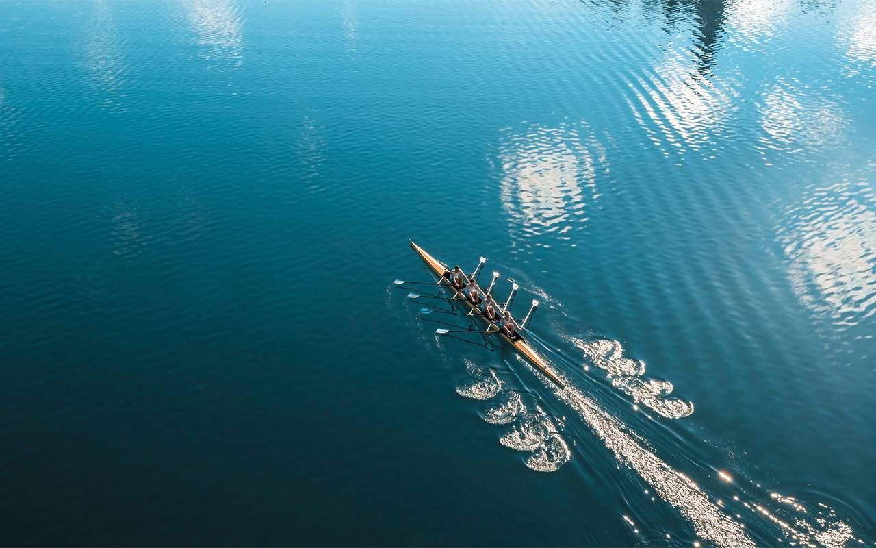 A rowing crew rows in a lake. Next Avenue, rowing after 50