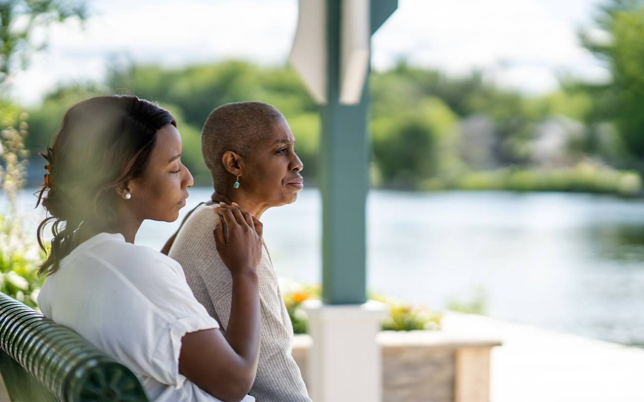 A young family caregiver sitting with her older mother on a park bench. Next Avenue