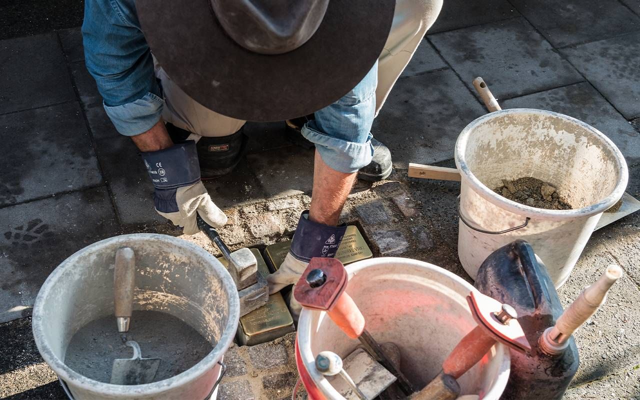 A person placing brass nameplate stones in the ground. Next Avenue, gunter demnig, stumbling stones