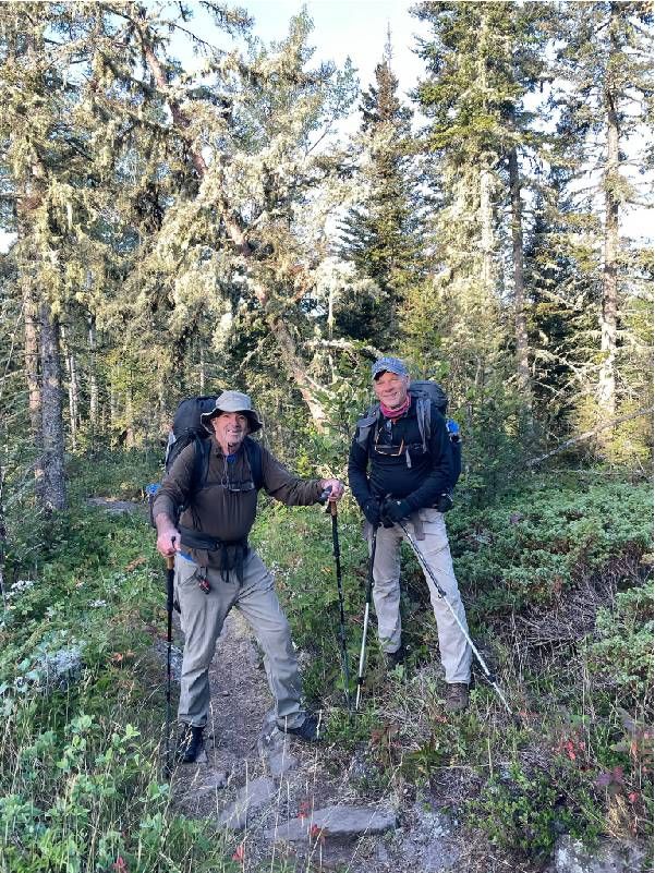 Two men with backpacking gear smiling on a hiking trail. Next Avenue