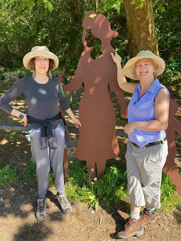 Two women standing next to a sculpture on a hiking trail. Next Avenue, Camino Trail