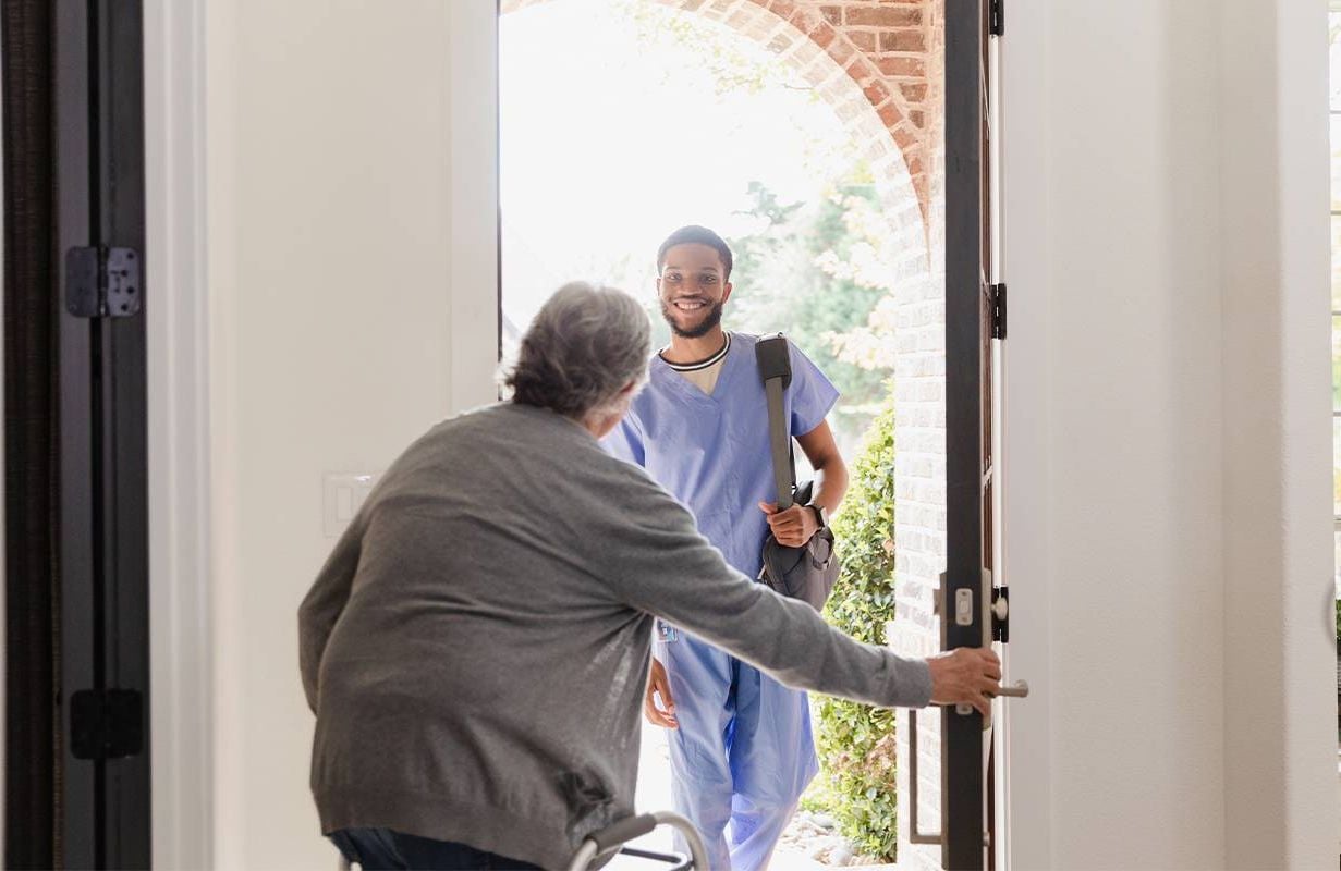 An older man opening the door for a hospice worker to come inside. Next Avenue