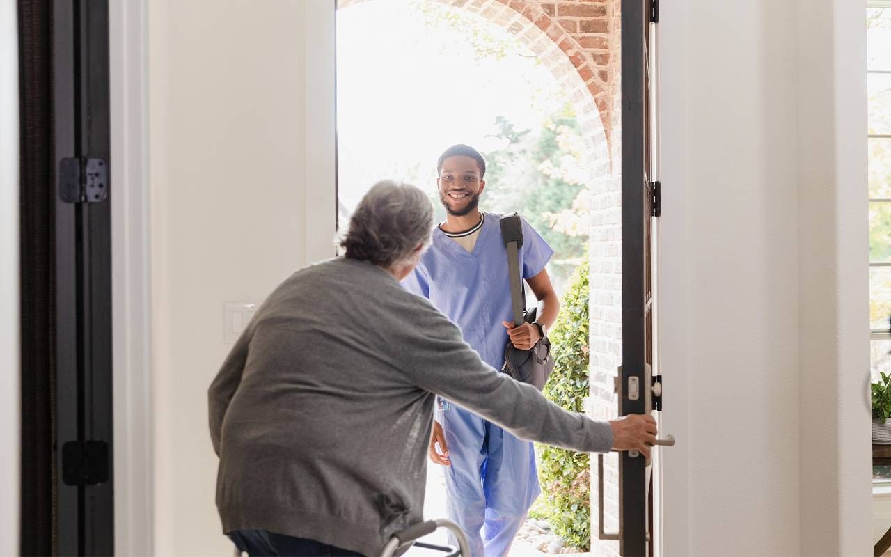 An older man opening the door for a hospice worker to come inside. Next Avenue