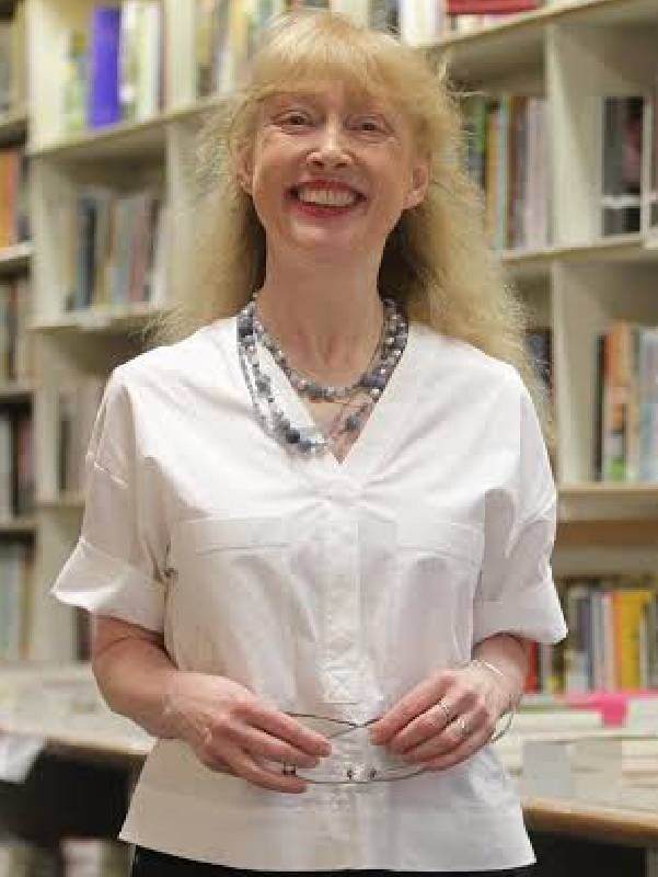 A person smiling in front of a bookshelf. Next Avenue