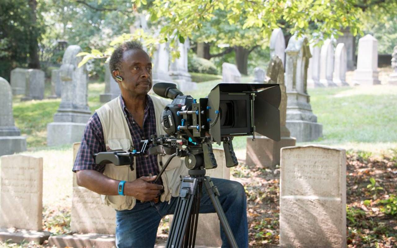 A man filming with a camera in a cemetery. Next Avenue