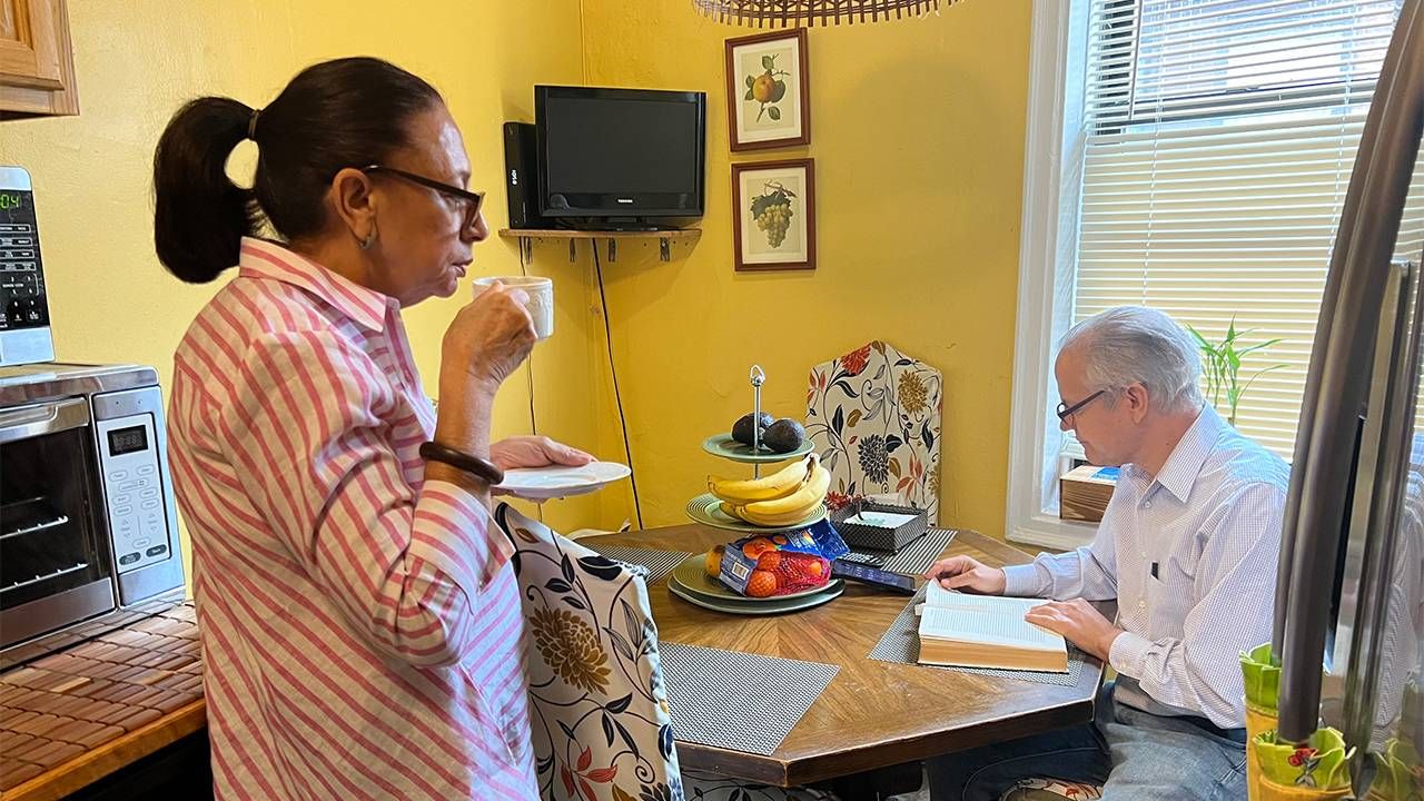 A man reading at the table and a woman sipping coffee. Next Avenue