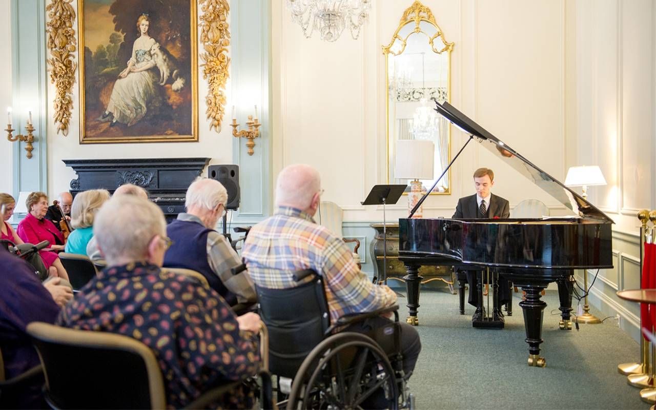 A young person playing piano to a crowd of older adults. Next Avenue