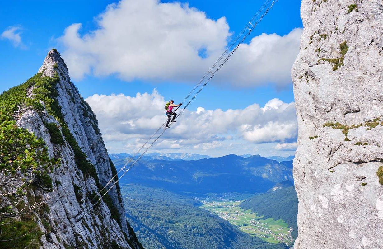 A person climbing down a suspended ladder between two mountains. Next Avenue