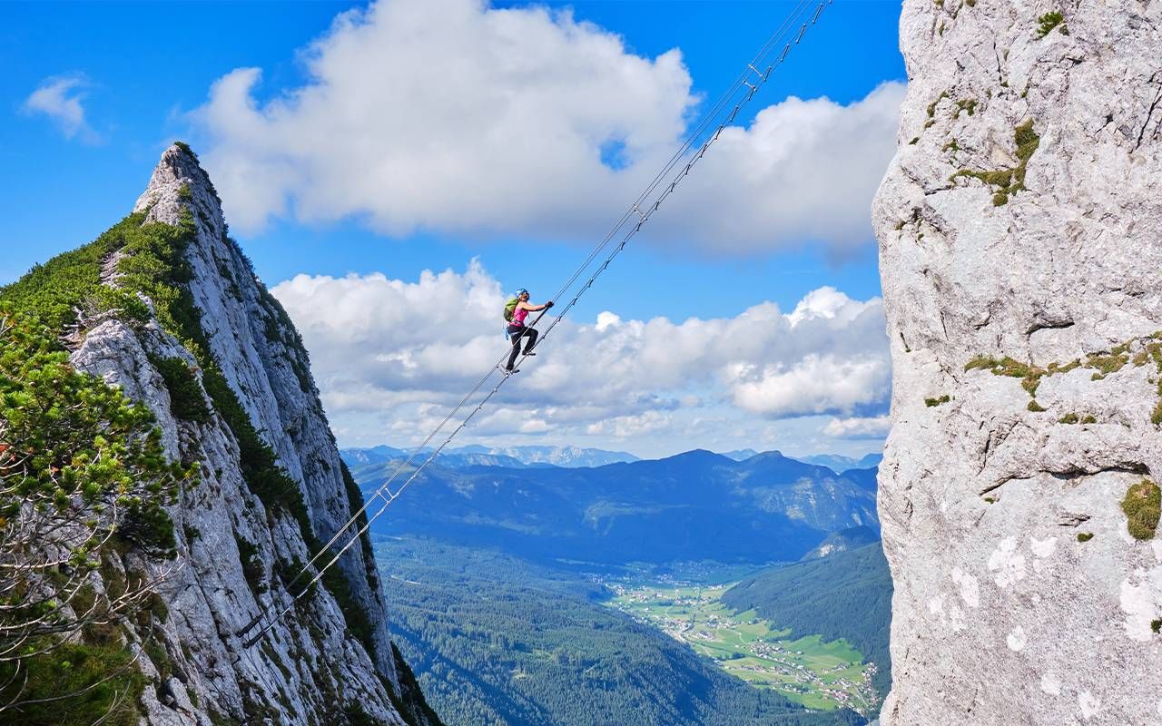 A person climbing down a suspended ladder between two mountains. Next Avenue