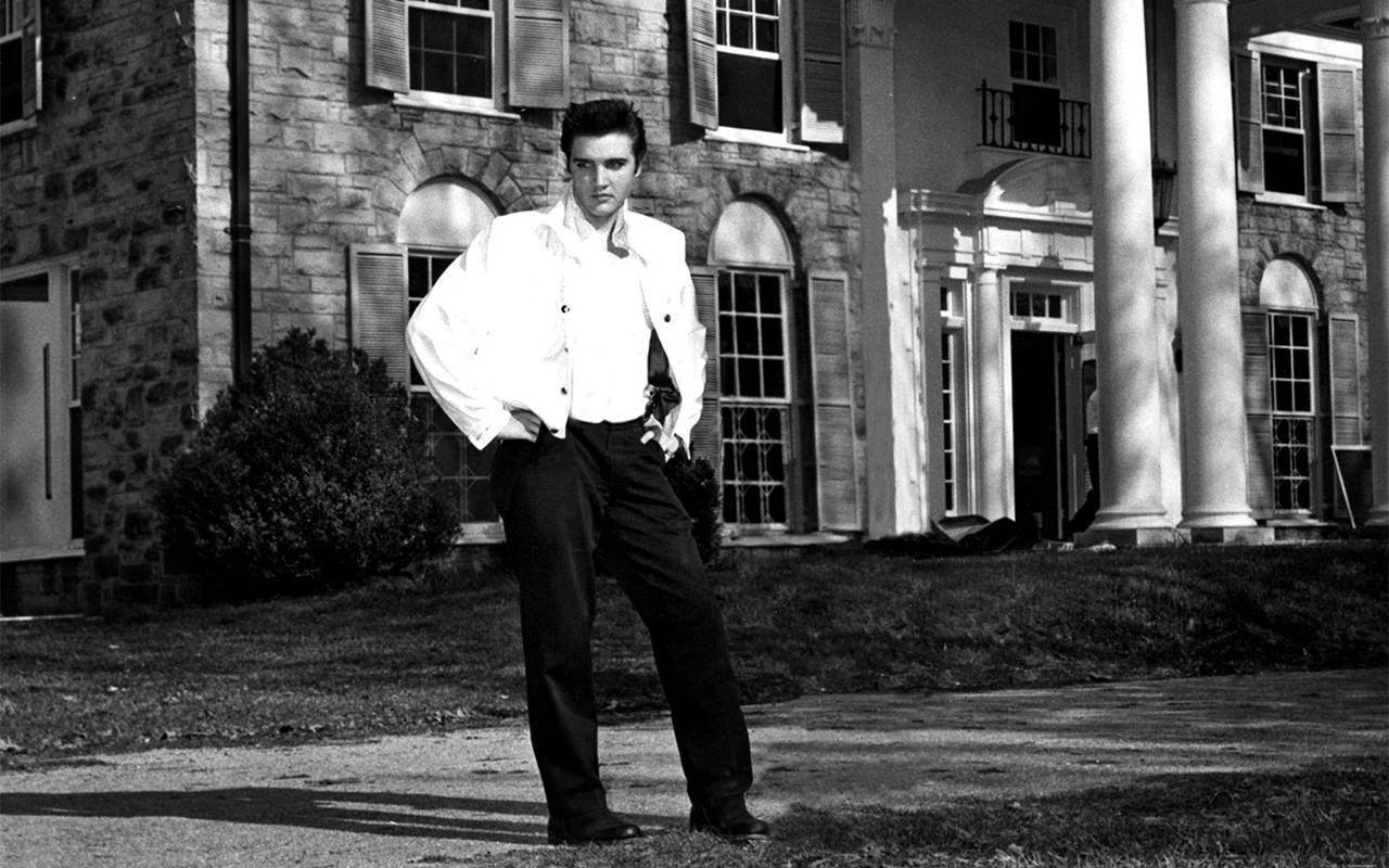 A black and white photo of Elvis standing outside of his home. Next Avenue