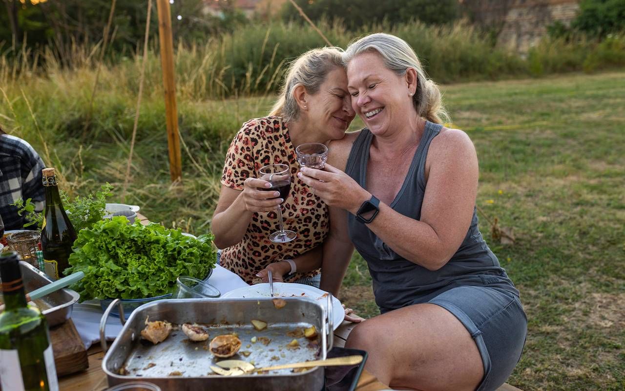 Two friends laughing together while sitting outside. Next Avenue