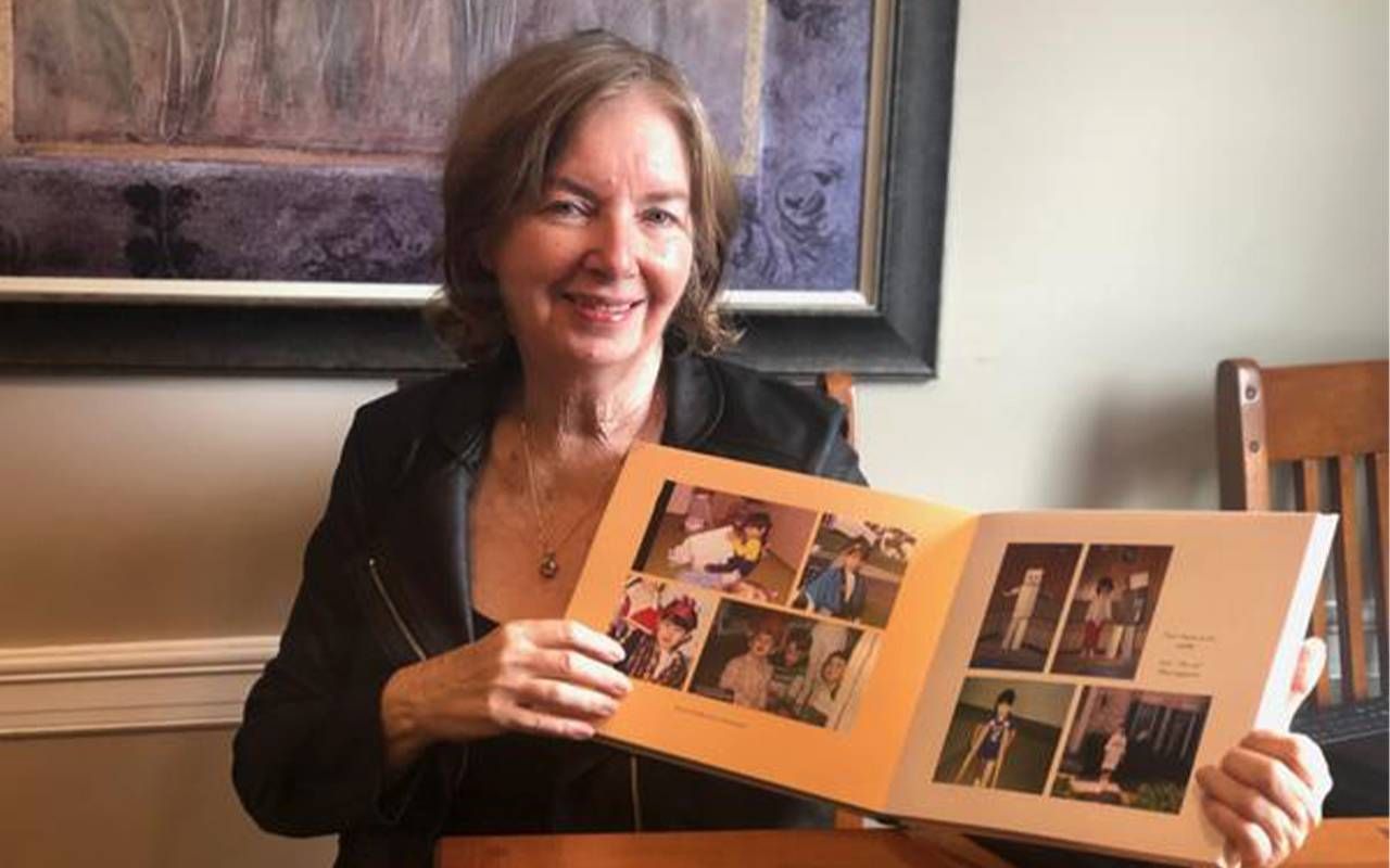 A woman sitting at a table holding a family photo album. Next Avenue