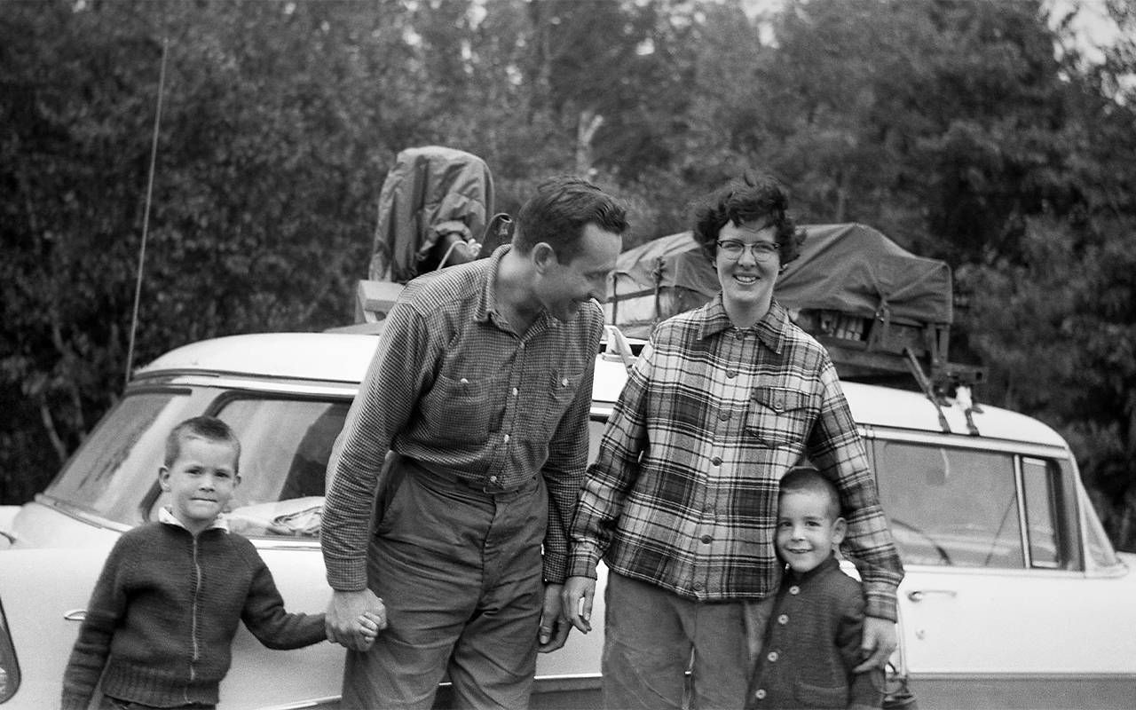 A family smiling outside of their station wagon while on a road trip. Next Avenue