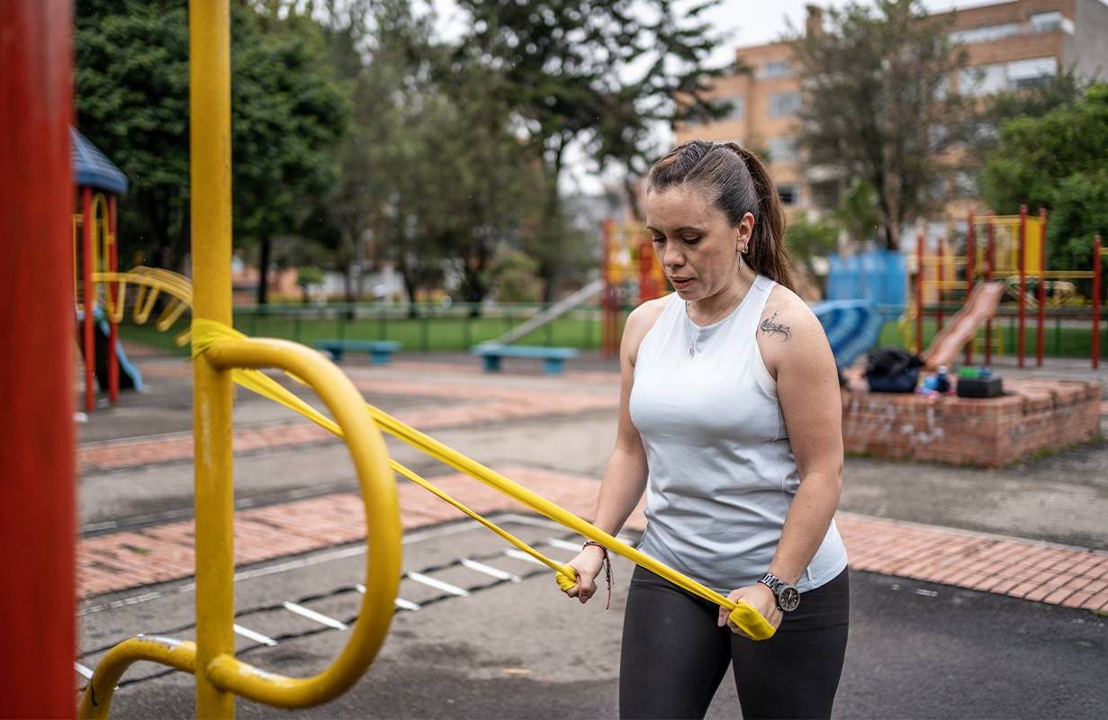 A woman using resistance bands doing strength training at a public park. Next Avenue