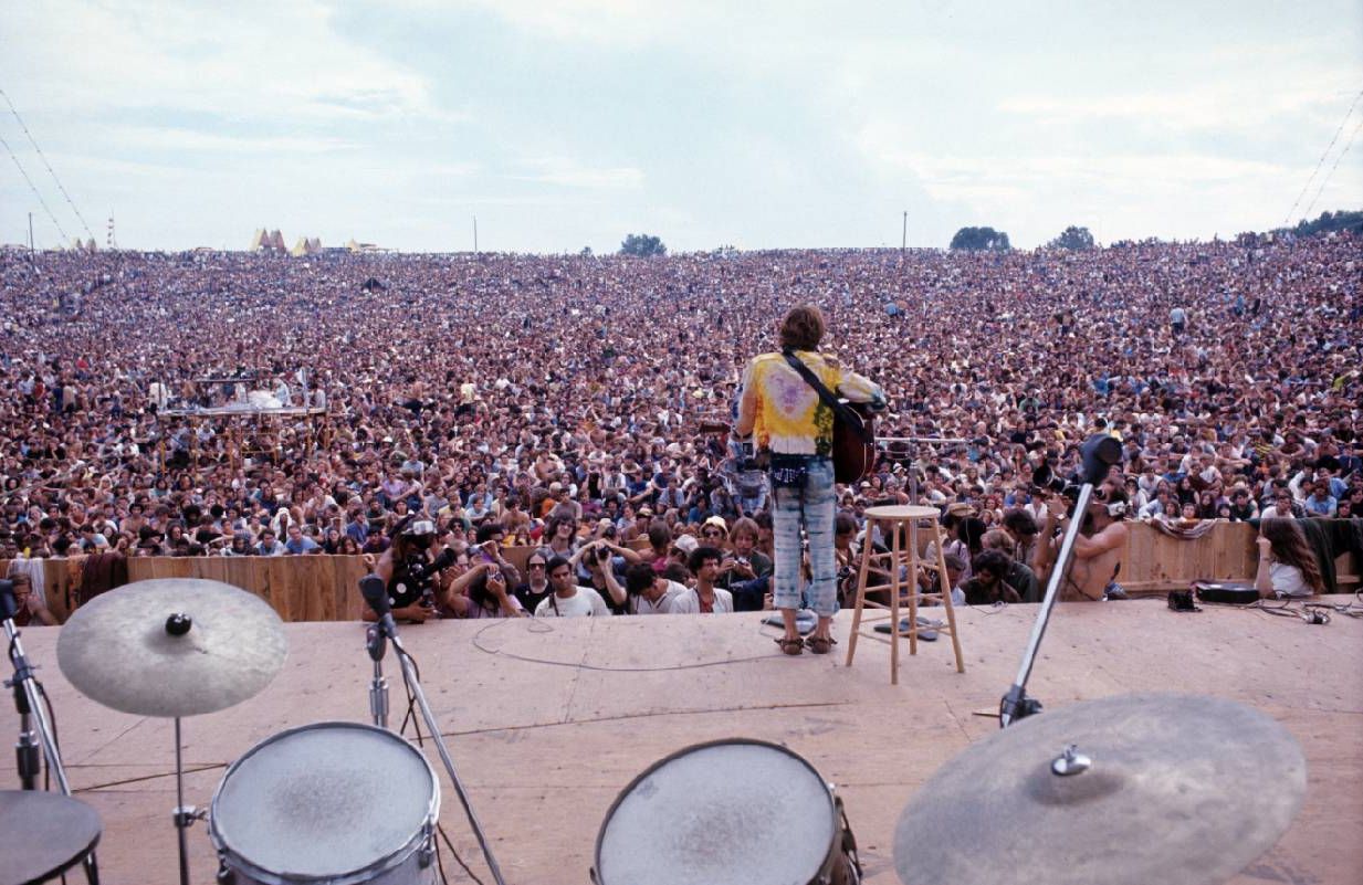 A man standing on a stage with a large crowd in front of him. Next Avenue, woodstock