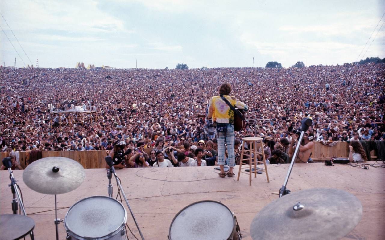 A man standing on a stage with a large crowd in front of him. Next Avenue, woodstock