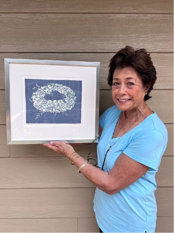 A woman holding up a framed print. Next Avenue