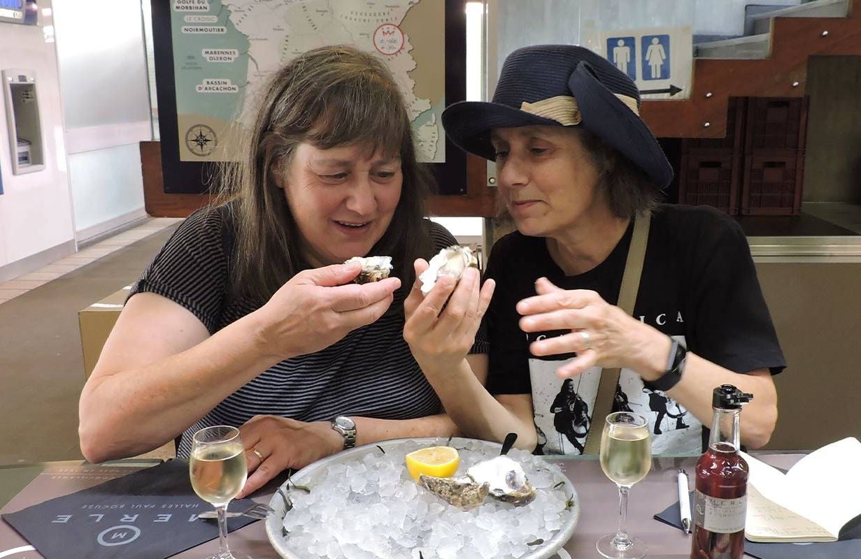 Sisters sitting next to each other and eating oysters. Next Avenue