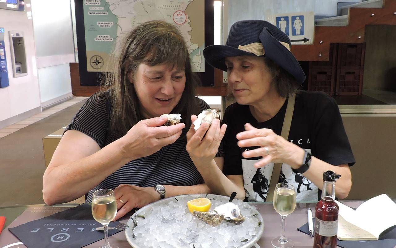 Sisters sitting next to each other and eating oysters. Next Avenue