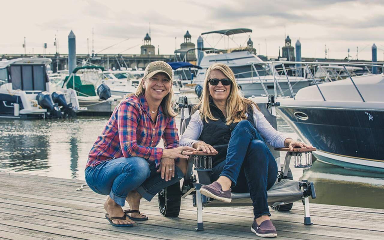 Two people smiling and sitting on a dock. Next Avenue