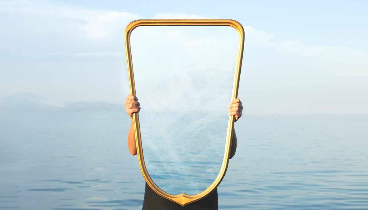 A person holing up a transparent mirror. Next Avenue
