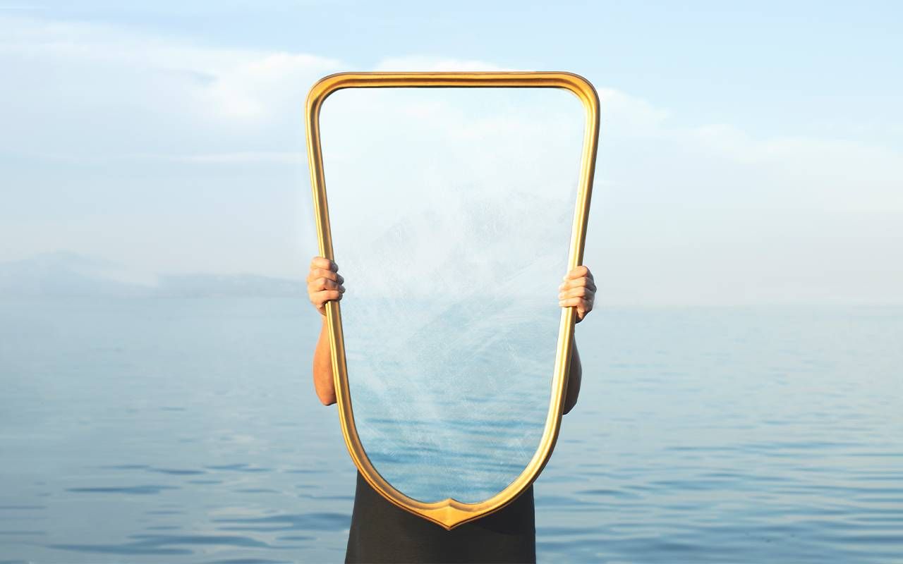 A person holing up a transparent mirror. Next Avenue