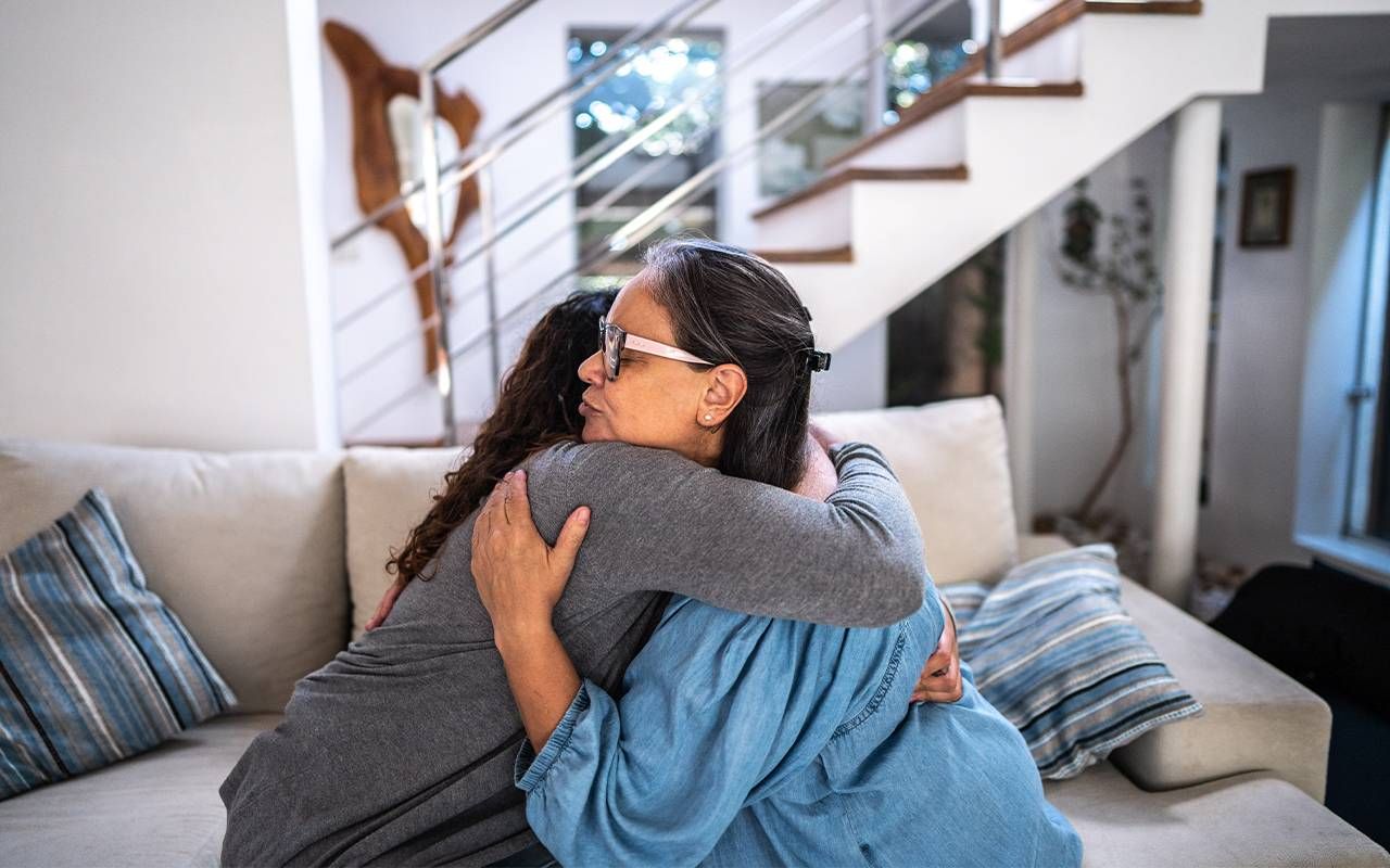 A mother and her daughter hugging on the couch at home. Next Avenue