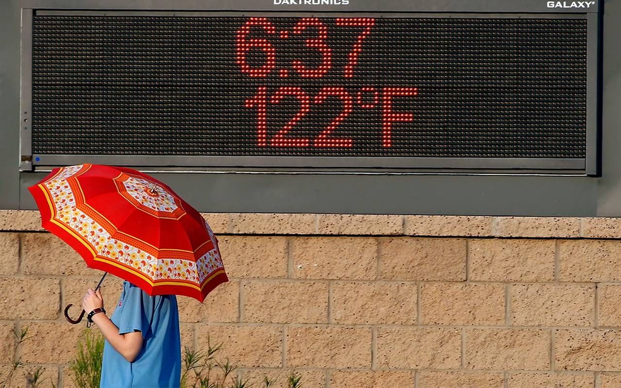A person with an umbrella walking underneath a sign that is displaying the temperature. Next Avenue, retirement, arizona