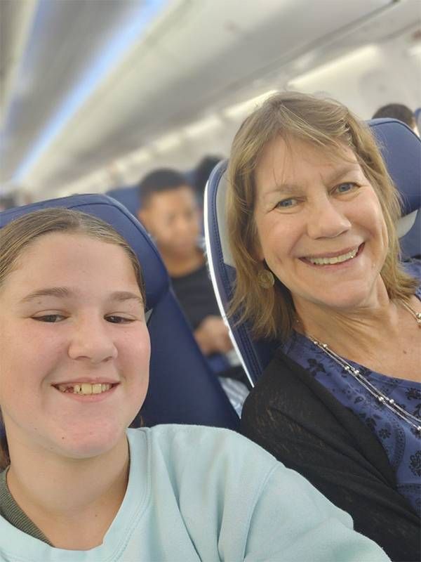 A grandmother and granddaughter smiling together on an airplane. Next Avenue